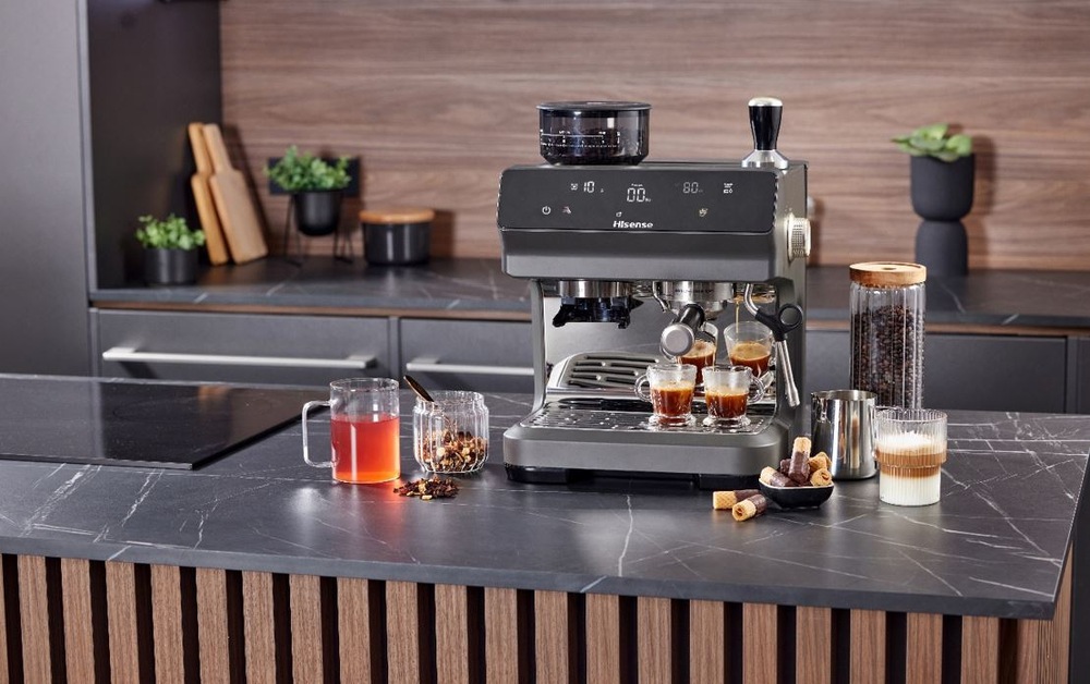 Espresso Hisense HSACM20LP antracitová farba pákový kávovar Hisense HSACM20LP na čiernej kuchynskej doske. Pripravuje dve epressá a vedľa stoji latte v pohári. Na druhej strane je čaj.