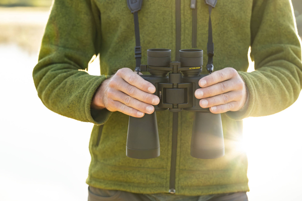 Detailný pohľad na ďalekohľad Nikon Action 7×50, ktorý má muž v zelenej mikine okolo krku.