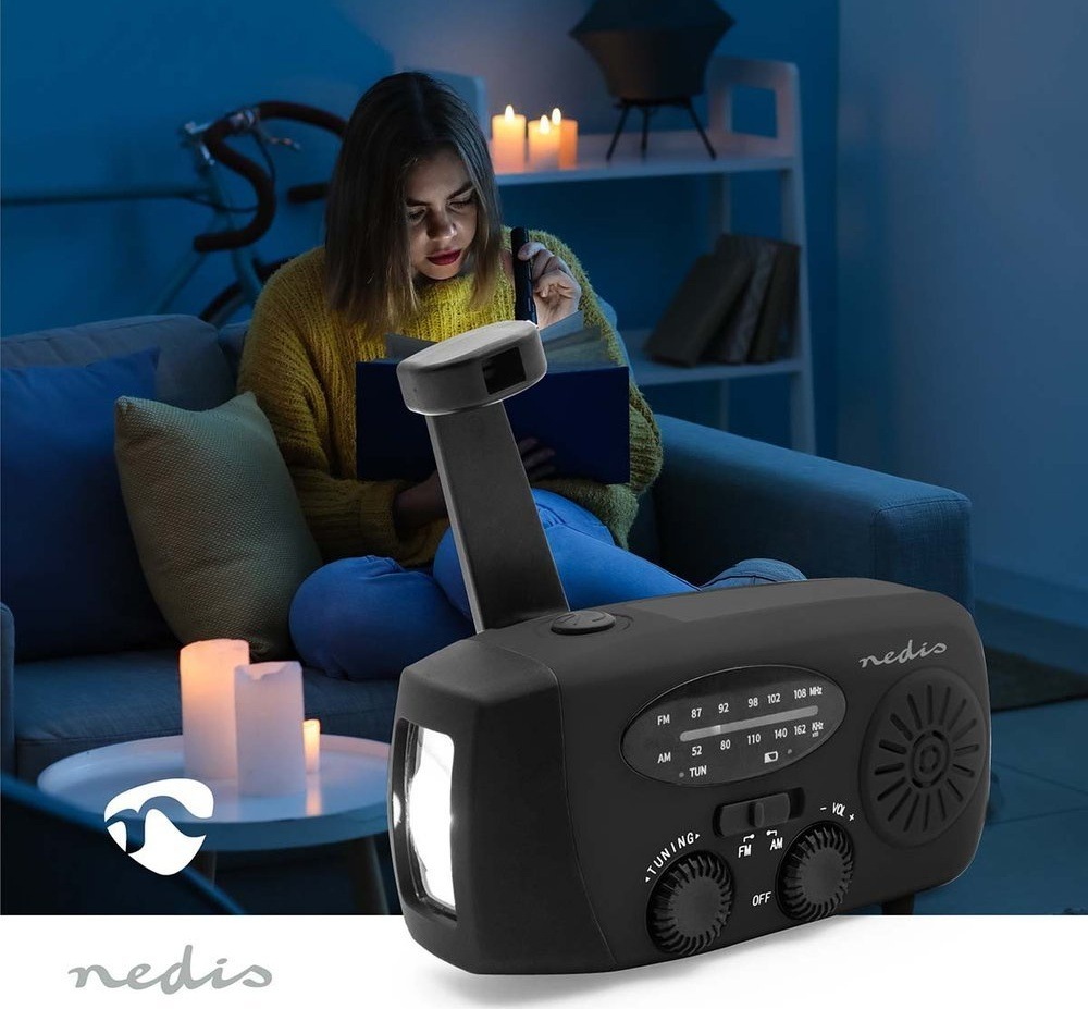 Rádioprijímač Nedis RDFMCR2000 čierny Žena číta pri výpadku prúdu za svitu sviečok, v popredí núdzové rádio Nedis so svietiacou baterkou.