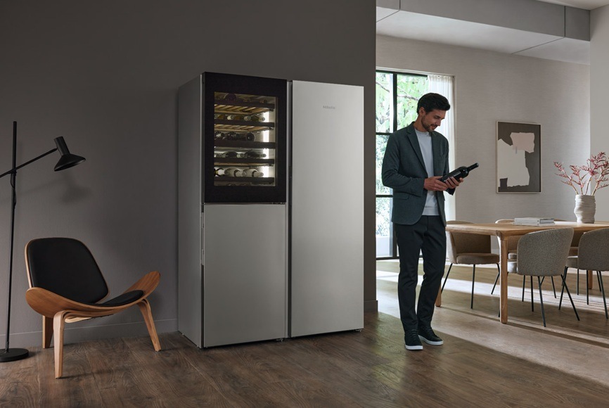 Vínotéka Miele KWNS 4784 DE Nerez/CleanSteel nerez Muž stojaci pred vinotékou a držiaci fľašu vína.