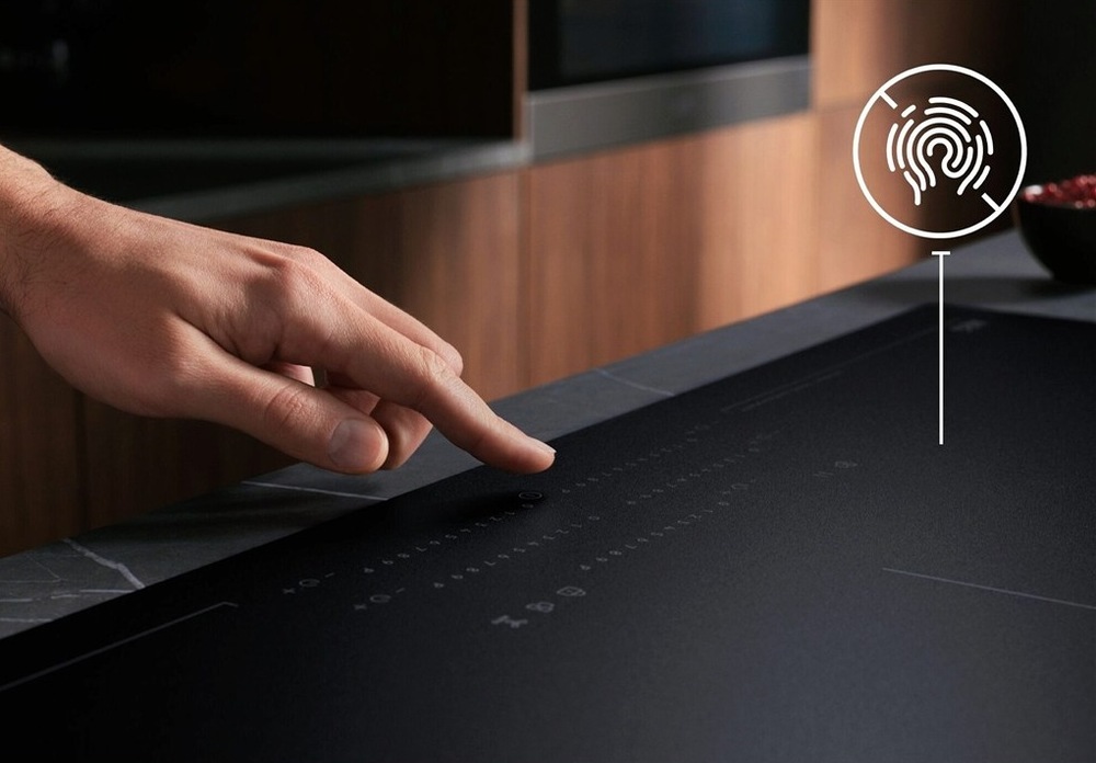Indukčná varná doska AEG série 7000 TI64IB10IZ SaphirMatt čierna Ruka nad ovládacím panelom matnej varnej dosky AEG. Vpravo hore je symbol znázorňujúci odolnosť voči odtlačkom prstov.