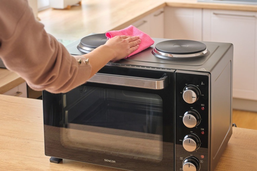 Mini rúra Sencor SEO 2800BK s hornými varnými platničkami pri čistení povrchu, v modernej kuchyni s dôrazom na jednoduchú údržbu a praktické ovládanie.