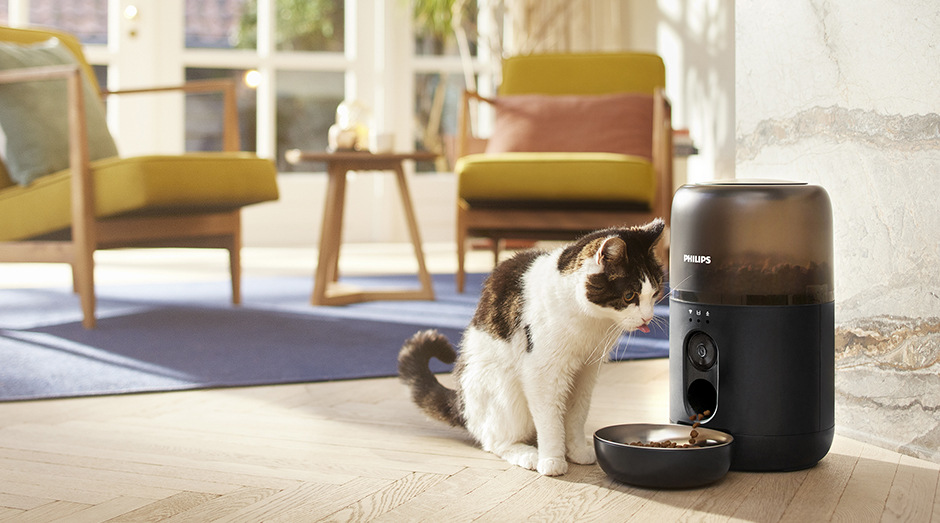 Chytré krmítko Philips a vedľa neho sediaca mačka, ktorá čaká na krmivo
