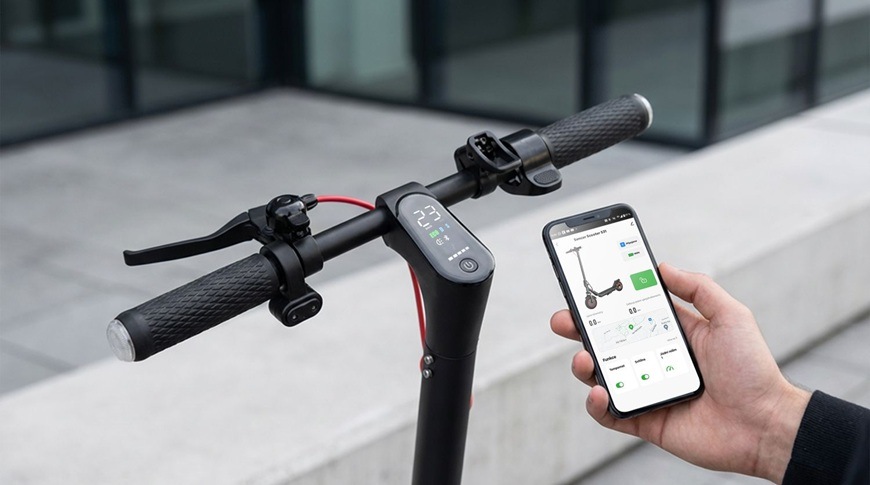 Elektrická kolobežka Sencor SCOOTER S31 čierna Detail riadidiel elektrickej kolobežky Sencor SCOOTER S31 s integrovaným displejom, ktorý zobrazuje aktuálnu rýchlosť a ďalšie údaje. Ruka vedľa drží chytrý telefón s aplikáciou Sencor HOME pre ovládanie kolobežky a sledovanie jej funkcií.