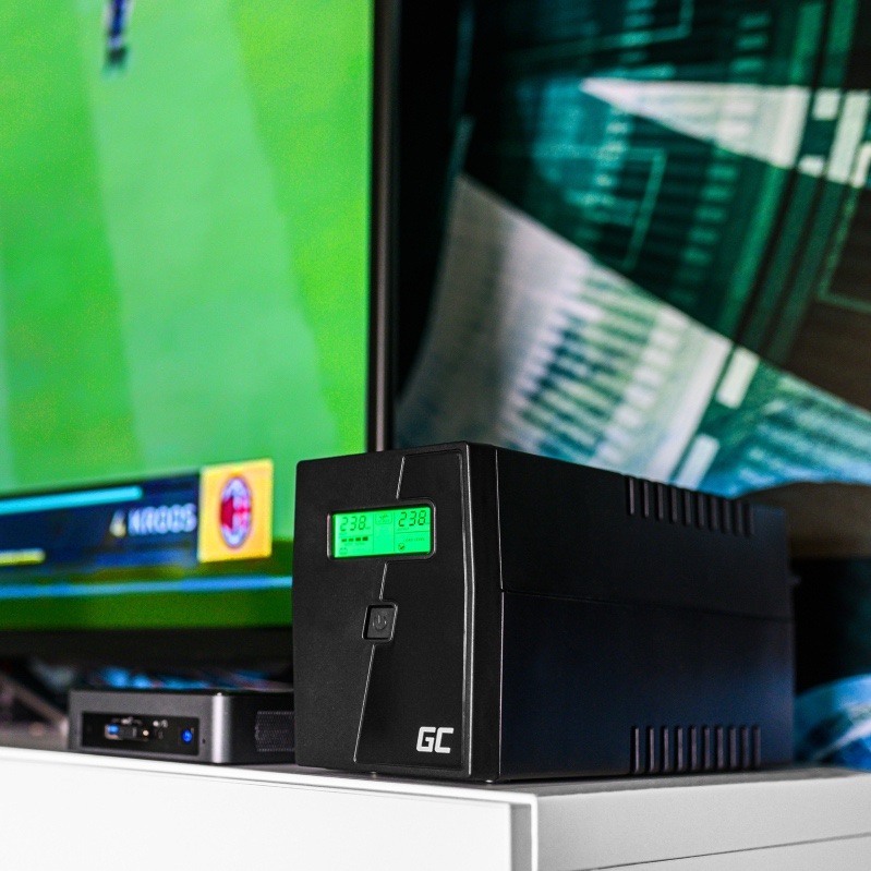 Záložný zdroj Green Cell Microsine 2000VA LCD čierny Na obrázku je záložný zdroj Green Cell Microsine postavený na bielej skrinke vedľa televízora. Má čierne hranaté telo, na čelnej strane zeleno svietiaci displej s prevádzkovými údajmi, pod ním tlačidlo zapnutia a dole logo GC. Vedľa neho leží menšie elektronické zariadenie av pozadí je rozmazaná televízna obrazovka so zeleným obrazom. Fotka ukazuje použitie zdroja v domácej zostave, napríklad pri televízii alebo multimediálnej technike.