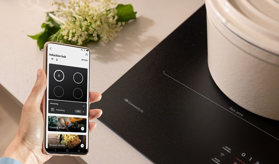 Indukčná varná doska Gorenje G600 GI6442MSCWF InfiniteMatt čierna ruka drží mobilni telefon u varne desky gorenje, se kterou je možno kounikovat. V telefonu je zapnuta aplikace ConnectLife.
