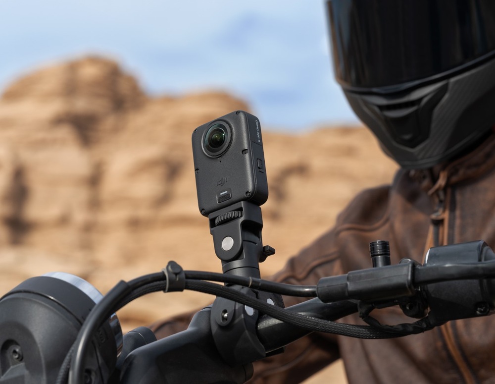 Outdoorová kamera DJI Osmo 360 II Limitless Riding Combo čierna Detail kamery DJI Osmo 360 upevnené na riadidlách motocykla, v pozadí sedí jazdec v helme