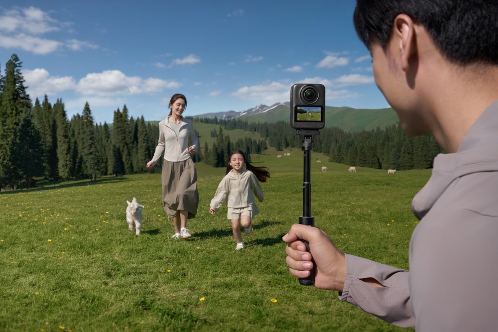 Outdoorová kamera DJI Osmo 360 II Standard Combo čierna Muž držiaci 360 ° kameru DJI Osmo 360 II na selfie tyči natáča ženu s dieťaťom bežiaci po horskej lúke