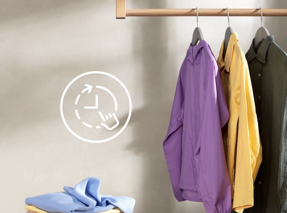 Práčka so sušičkou Electrolux EW5W468WE biela Na ramienku visí fialová bunda, žltá a khaki košeľa. Vľavo symbol pre funkciu TimeManager.
