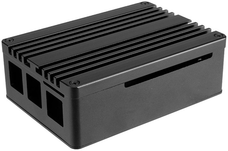 Na snímke je vidieť čelnú a ľavú stranu puzdra v čiernom pieskovanom eloxovanom hliníku. V popredí vynikajú obdĺžnikové výrezy pre porty Raspberry Pi (USB, HDMI, Ethernet atď.), ktoré sú presne zarovnané s hranou puzdra. Nad týmito výrezmi je dobre viditeľný malý otvorený prístup k microSD slotu, ktorý je čiastočne zakrytý konštrukciou puzdra, ale stále dobre prístupný.