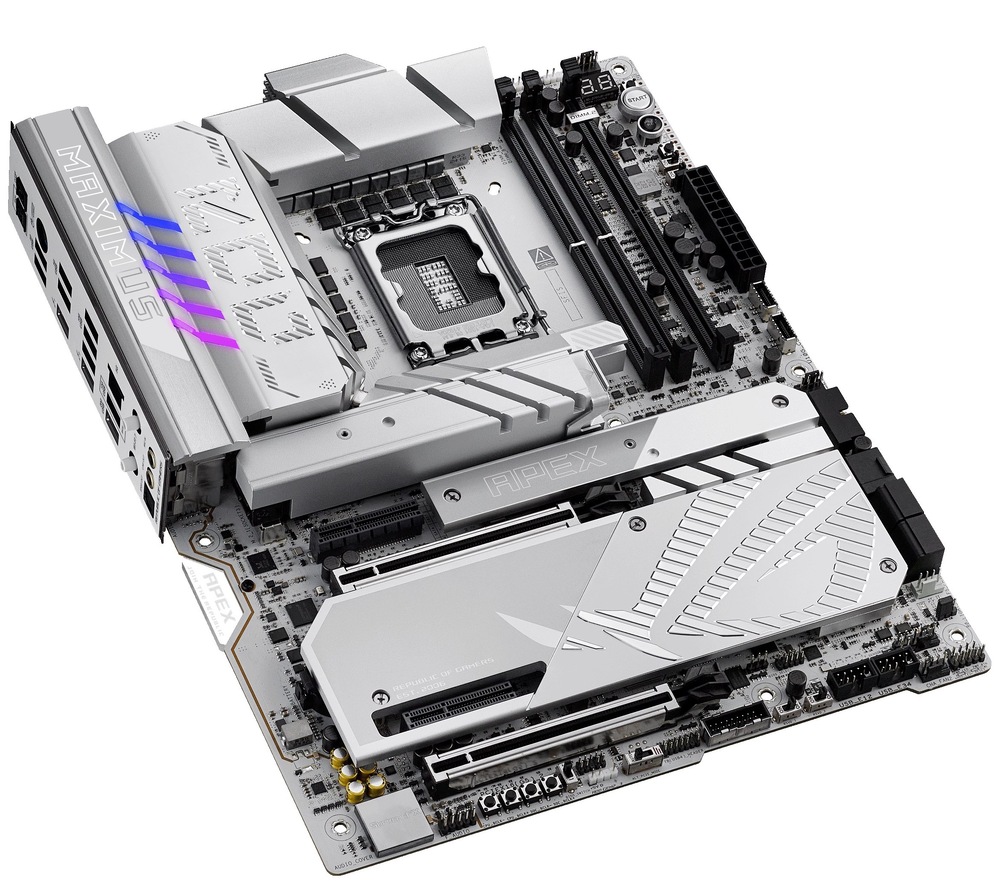 Základná doska Asus ROG MAXIMUS Z890 APEX Na fotke je doska fotená zhora pod miernym uhlom z pravej strany, takže je vidieť hlavne jej „povrch“ a vrstevnaté chladiče. Dominuje strieborno-biele prevedenie s veľkými pasívami okolo pätice procesora uprostred a dlhými krytmi pre M.2/čipset v spodnej časti. Vpravo hore sú dva DDR5 sloty a pri hornej hrane napájacie konektory. Na ľavom okraji je ľahko vidieť aj zadný panel (I/O) – kovový blok s portami je len čiastočne „vykuknutý“ do záberu.
