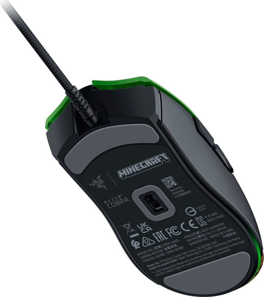 Myš Razer COBRA Lightweight Wired Minecraft Ed. zelená Na obrázku je spodná strana drôtovej hernej myši Razer Cobra Minecraft Edition. Myš má čierno-zelené prevedenie, opletený kábel a na spodnej časti je vidieť optický senzor uprostred. Okolo senzora sú šedé klzné plôšky na hladký pohyb po podložke. Na tele sú tiež logá Razer Cobra, Minecraft a technické údaje produktu. Na boku sú čiastočne vidieť bočné tlačidlá.