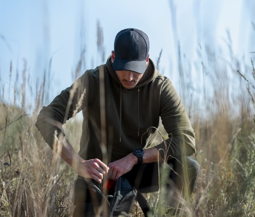 Inteligentné hodinky Garmin Instinct 3 - 50 mm AMOLED - Tactical Edition čierne Muž vo vysokej tráve sleduje displej hodiniek Garmin Instinct 3 – 50 mm, AMOLED, Tactical Edition