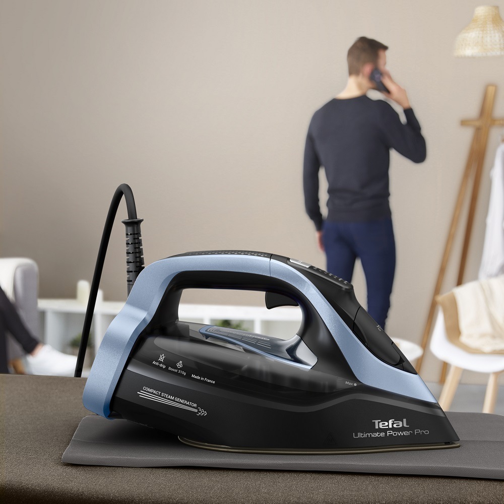 Žehlička Tefal Ultimate Power Pro FV9E53E0 čierna/modrá Muž telefonuje a na žehliacej doske nechá položenú žehličku Tefal FV9E53E0 Ultimate Power Pro, ktorá sa sama vypne