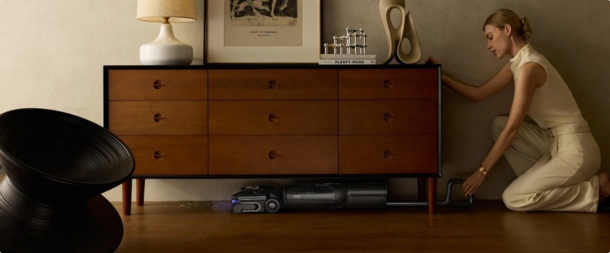 Čistič tvrdých podláh Roborock F25 Ultra čierny Žena vysáva s tyčovým vysávačom Roborock F25 Ultra pod modernou komodou.