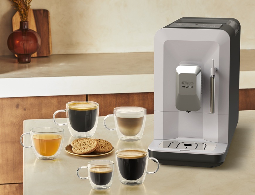 Automatický kávovar Krups EA201BE0 My Coffee Steam čierny/svetlo šedá Automatický kávovar Krups EA201BE0 My Coffee Steam je položený na kuchynskej linke. Vedľa neho sú sklenené šálky s rôznymi kávami a čajom. Na tanieriku sú sušienky. V pozadí je vidieť zvyšok kuchyne.