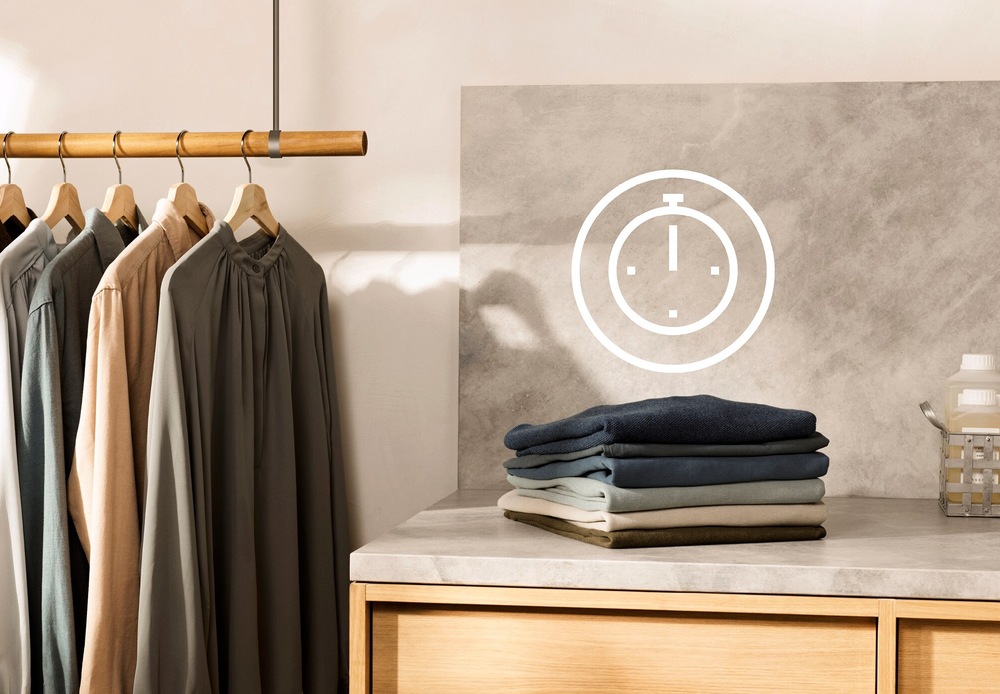 Práčka Electrolux SensiCare 600 EW6T836C biela Symbol úspory času nad kôpkou poskladanej bielizne. Vľavo košele zavesené na ramienku.