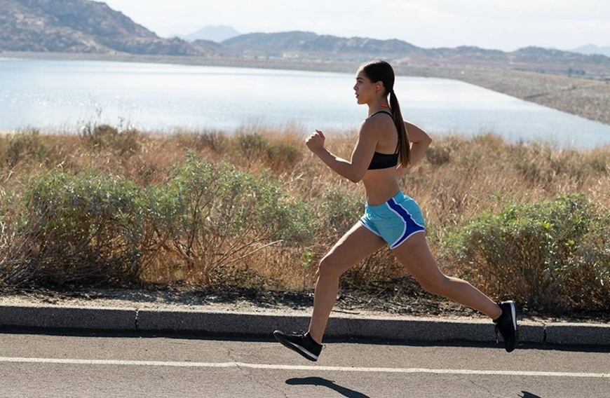 Slúchadlá JBL Endurance Run 3C čierna/sivá Žena bežiaca pozdĺž vody s nasadenými slúchadlami.