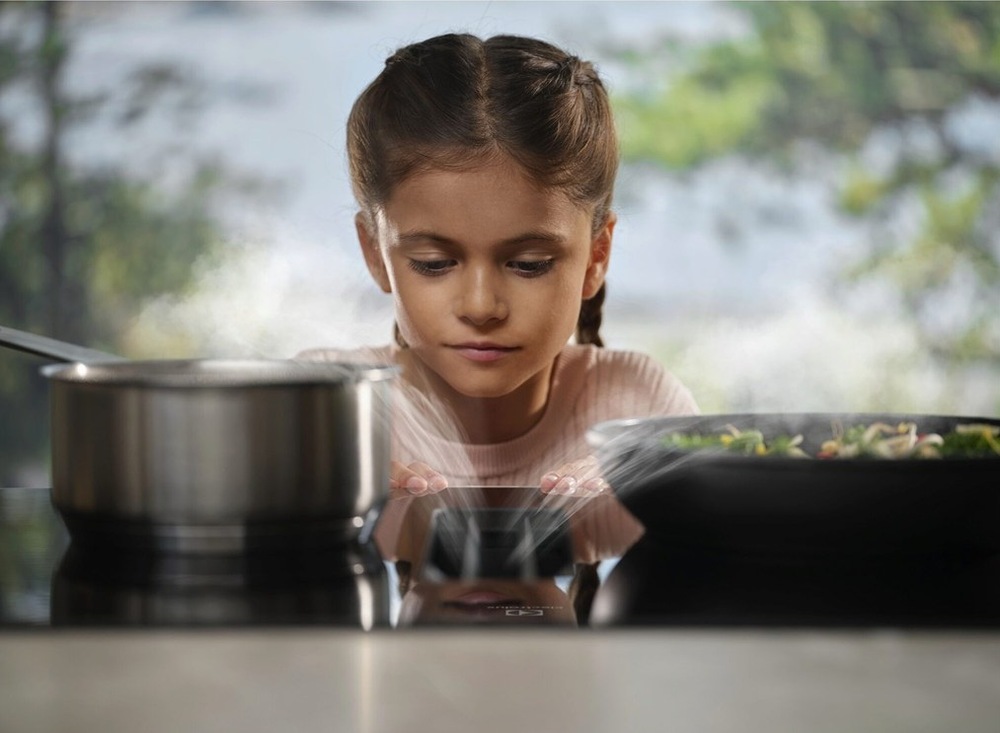 Indukčné varné dosky s odsávaním Electrolux Série 600 ECC63410CT SaphirMatt SE čierna Dievčatko sleduje paru miznúcu v odsávači pár dosky Electrolux.