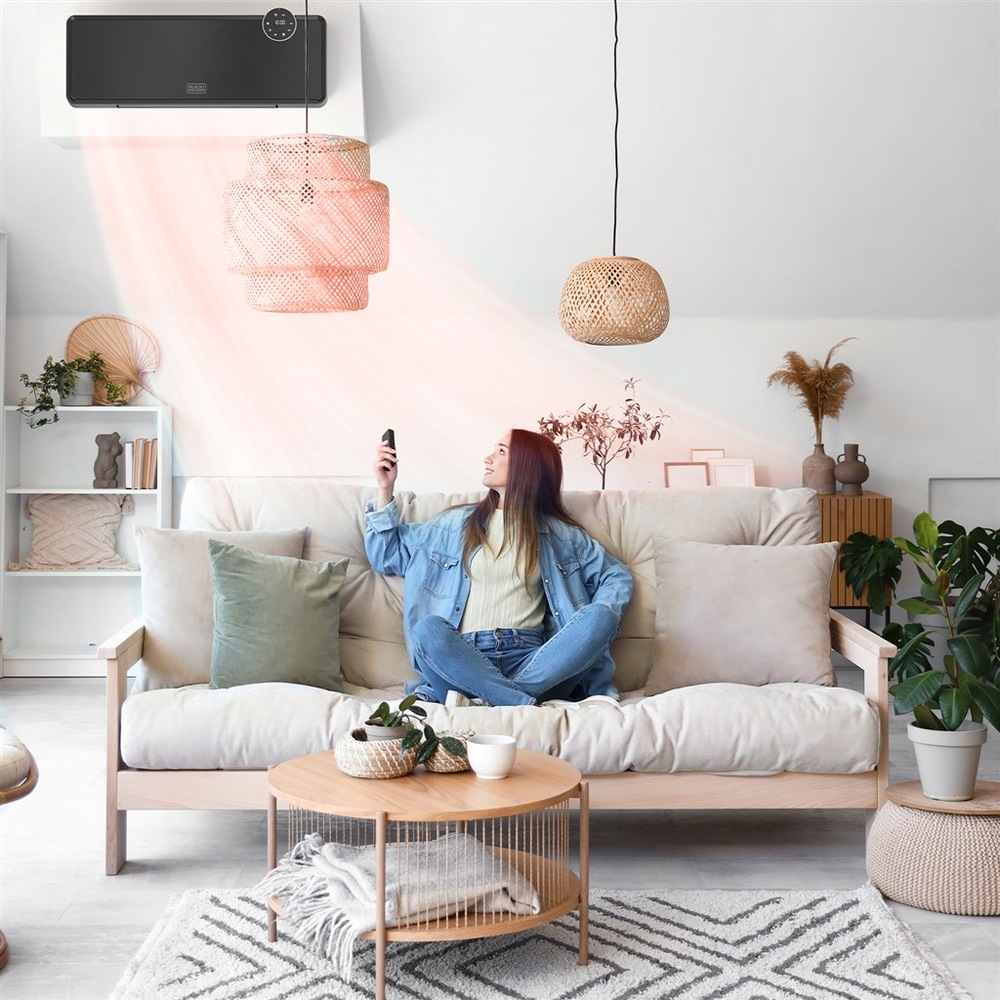 Žena sedí na gauči, v ruke ovládačom mieri na vykurovací panel Black+Decker