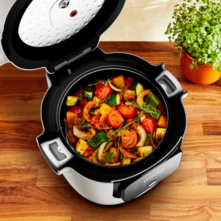 Otvorený multifunkčný hrniec Tefal MY700BF0 Multicook pripravuje farebnú zmes pečenej zeleniny s paradajkami cuketou a paprikou na drevenej kuchynskej linke.