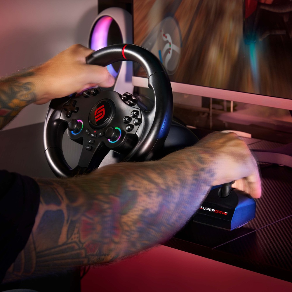 Volant SUPERDRIVE 220 RS-X čierny Na zábere tetovanej paže používateľa drží herný volant a radiacu páku. Na monitore sa zobrazuje závodná hra vytvárajúca intenzívnu a pohlcujúcu atmosféru.