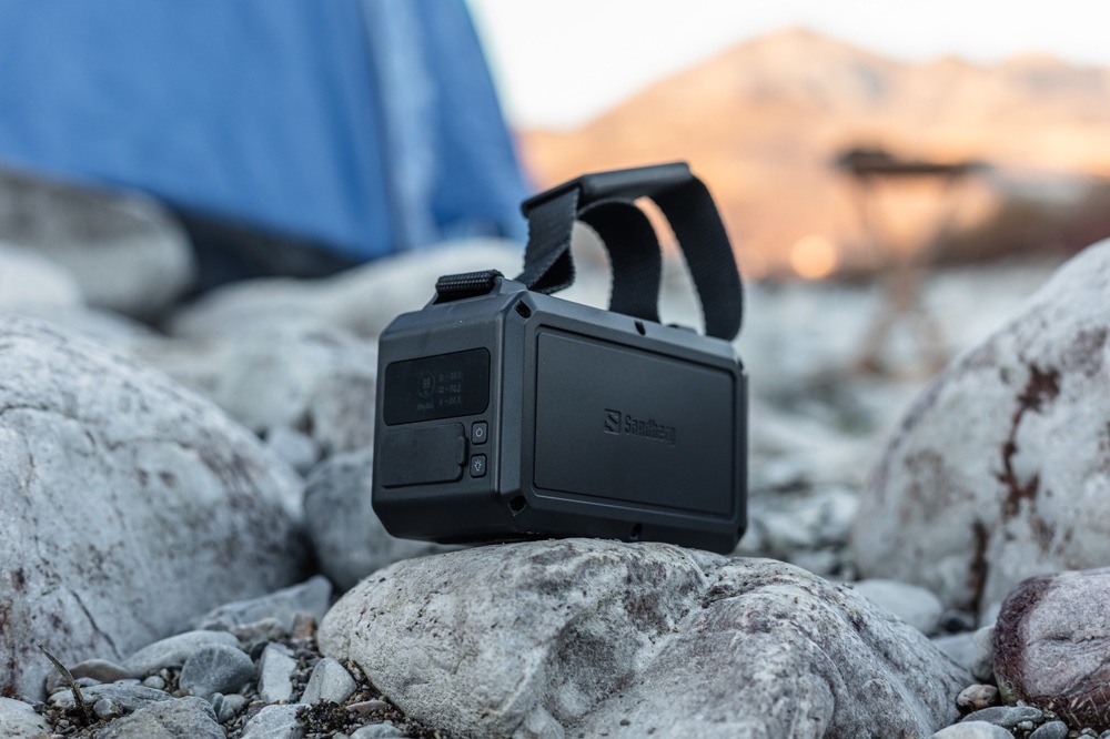 Powerbank Sandberg Survivor 40000 mAh PD 100W čierny Powerbanka Sandberg Survivor 100W 40000 s držadlom umiestnená na kameňoch vedľa stanu.