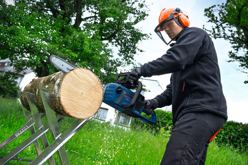 Reťazová píla Bosch Professional GKE 18V-40 pri rezaní kmeňa na stojane v exteriéri
