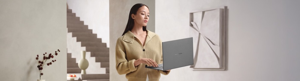 Notebook Asus Zenbook S16 sivý Žena drží v ruke otvorený Zenbook S16 s prémiovým dizajnom pre prácu, štúdium aj každodenné používanie