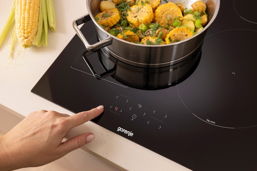 Dotykové ovládanie indukčnej varnej dosky Gorenje GI6431BFG pri varení zeleniny v hrnci v modernej kuchyni.