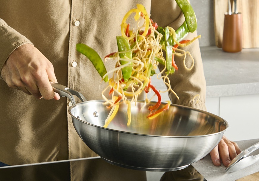 Panvica WOK Tefal Extreme E5291904, 28 cm nerez Muž vo WOK panvici premiešava kúsky zeleniny.