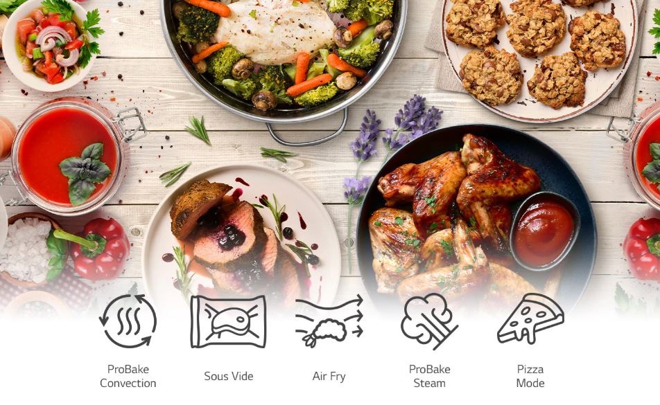 Rúra LG WSED7667M čierna na stole ležia pripravené pokrmy z rúry LG, ktorá ponúka mnoho programov pre rôzne typy prípravy: Sous Vide, Air Fry, Para, Pizza,... Na obrázku vidíme rajskú polievku s bazalkou, zapečenú brokolicu so zeleninou, šťavnaté mäso s brusnicami, pečené kuracie krídla alebo ovce.