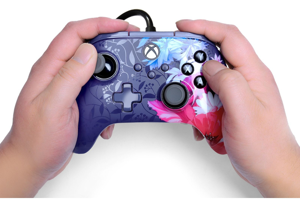 Gamepad PowerA Advantage Plus - Xbox fialový Na obrázku drží človek oboma rukami herný ovládač PowerA Advantage Plus počas hrania. Palce spočívajú na analógových páčkach a tlačidlách, čo ukazuje bežný spôsob ovládania hier. Dobre sú vidieť tlačidlá A, B, X a Y, smerový kríž, funkčné tlačidlá uprostred aj tlačidlo s logom Xbox. Snímka demonštruje ergonomický tvar ovládača, vďaka ktorému pohodlne padne do rúk aj pri dlhšom hraní.
