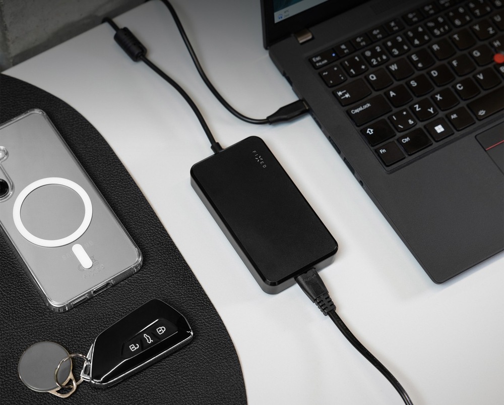 Sieťový adaptér FIXED GaN USB-C, PD 3.0, 100 W čierny Nabíjací adaptér FIXED GaN USB-C, PD 3.0, 100 W vedľa notebooku a telefónu