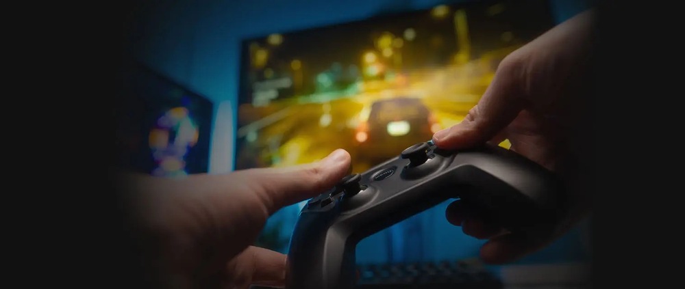 Herný monitor MSI MAG 274CF X24 čierny Detailný záber rúk držiacich herný ovládač pred rozmazanou obrazovkou zobrazujúcou závodnú hru. Scéna vyjadruje sústredenie a vzrušenie.