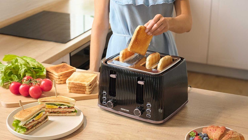 Žena pripravuje raňajky a vyťahuje toast z hriankovača Sencor v modernej svetlej kuchyni.