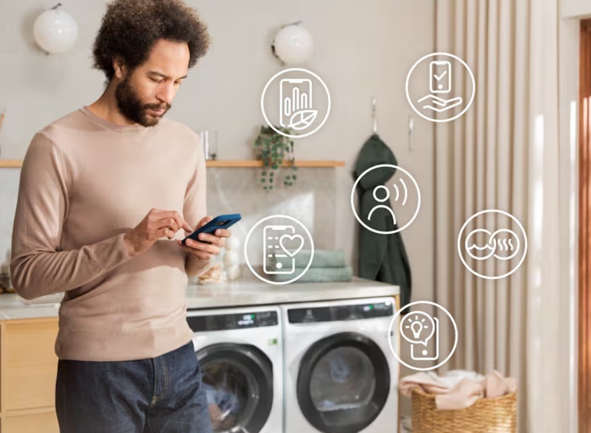 Sušička bielizne Electrolux série 800 EW8D595RCDC ocel Muž ovláda sušičku Electrolux pomocou mobilnej aplikácie. Okolo sú symboly jednotlivých funkcií.