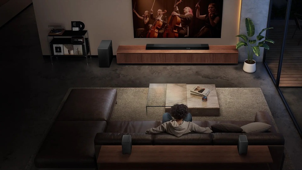 Soundbar Hisense AX5140Q čierny Muž sedí na gauči v obývacej izbe a pozerá sa na televíziu, kde dávajú záznam z koncertu.