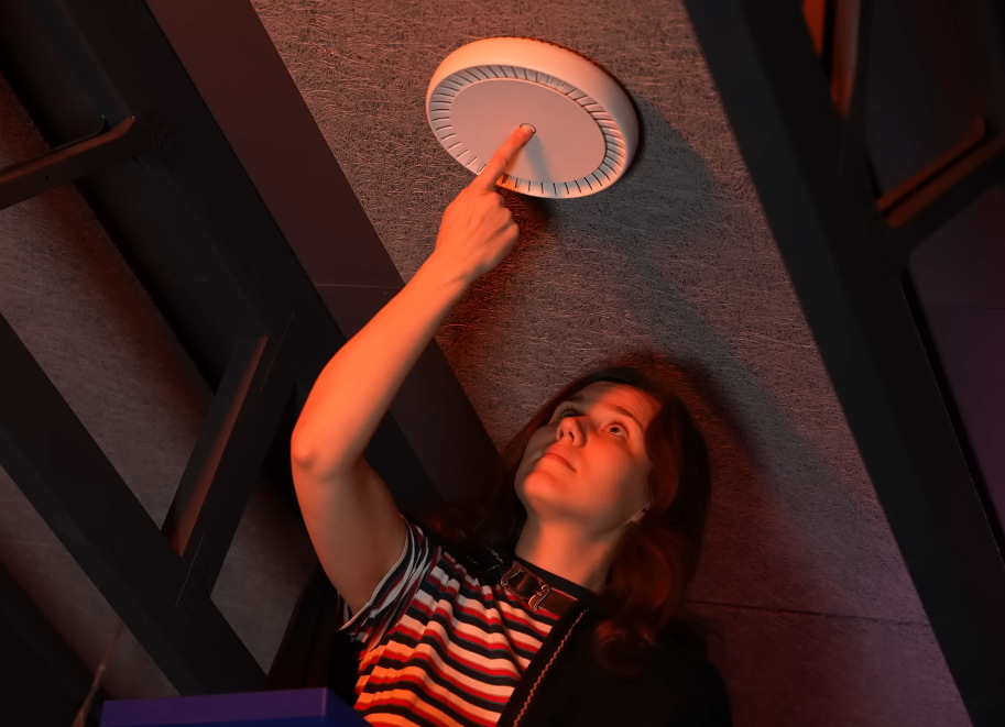 Prístupový bod (AP) MikroTik cAPGi-5HaxD2HaxD biely Žena stláčajúca tlačidlo na stropnom access pointe MikroTik pri inštalácii.