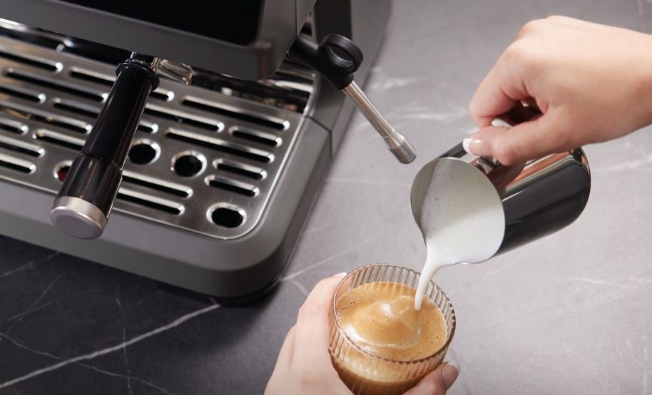 Espresso Hisense HSACM20LP antracitová farba ženská ruka prelieva našľahané mlieko z kanvičky do pripravenej kávy v kávovare Hisense HSACM20LP