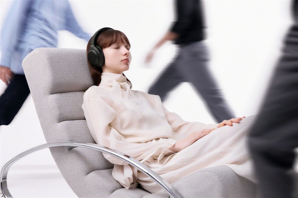 Slúchadlá Sony WH-1000XM4C čierna žena so slúchadlami Sony WH-1000XM4C pri počúvaní hudby v kresle