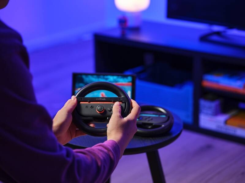 Volant Trust GXT 1257, Nintendo Switch 2, 2 ks čierny Hráč drží volant Trust GXT 1257 s vloženým ovládačom pri hraní závodnej hry v obývačke