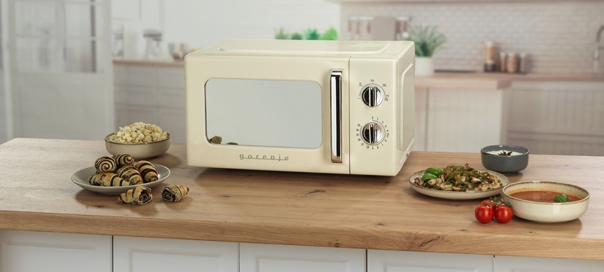 Mikrovlnná rúra Gorenje Retro MO20E1HRL béžová Retro mikrovlnná rúra Gorenje MO20E1HRL má pootvorené dvierka. Je umiestnená na kuchynskej linke a okolo nej sú rôzne potraviny.