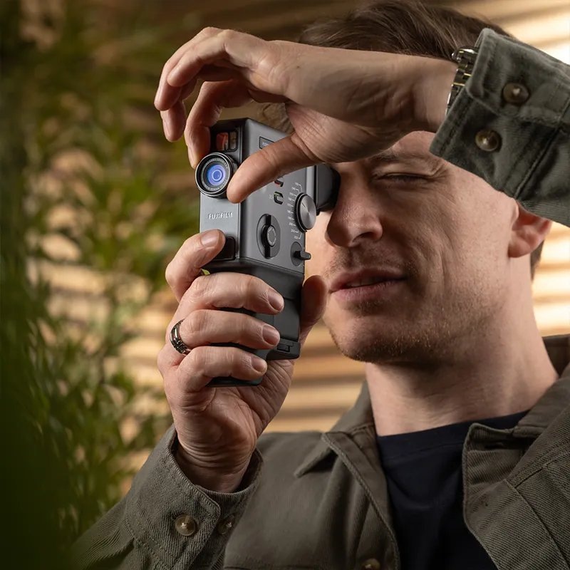 Instantný fotoaparát Fujifilm Instax mini EVO Cinema čierny Muž používajúci hľadáčik instantného fotoaparátu Instax mini EVO Cinema a krúžok objektívu