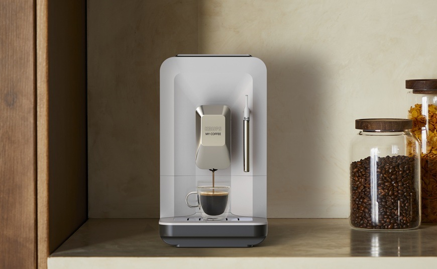 Automatický kávovar Krups EA201BE0 My Coffee Steam čierny/svetlo šedá Čelný pohľad na automatický kávovar Krups EA201BE0 My Coffee Steam, ktorý je položený na linke. Vedľa neho sú dózy s kávovými zrnami.
