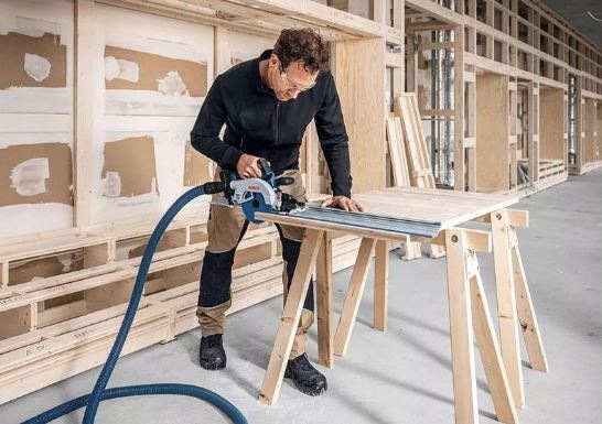 Okružná píla Bosch Professional GKS 18V-57-2 GX (bez baterie) Muž v dielni pracuje s okružnou pílou a využíva systém odvádzania prachu pre bezprašné pracovné prostredie.