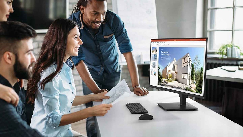 Rôznorodá skupina kolegov, ktorí sa usmievajú a pozerajú na monitor zobrazujúci architektonické návrhy. Svetlé, moderné kancelárske prostredie.