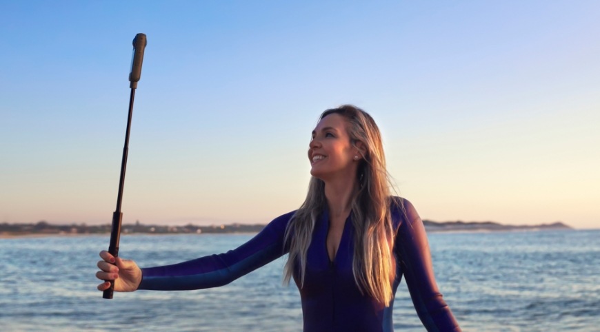 Žena stojaca na pláži si kupuje selfie pomocou akčnej kamery a selfie tyče Insta360 114 cm