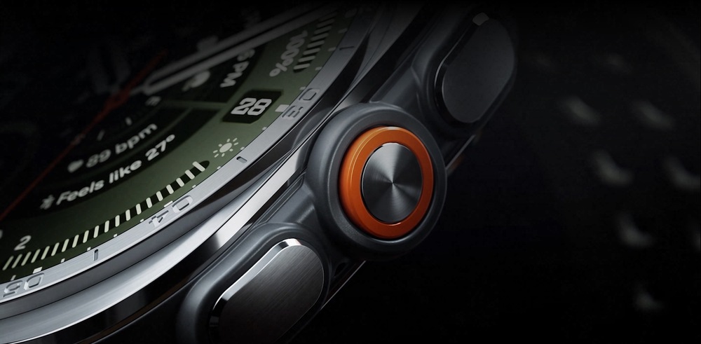 Detailný záber na odvážne navrhnuté, intuitívne tlačidlá a oranžové Akčné tlačidlo na bočnej strane hodiniek Galaxy Watch Ultra2 vo farebnom prevedení Titanium Silver so športovým remienkom Marine Band vo farbe Olive zobrazenej v miernom uhle.