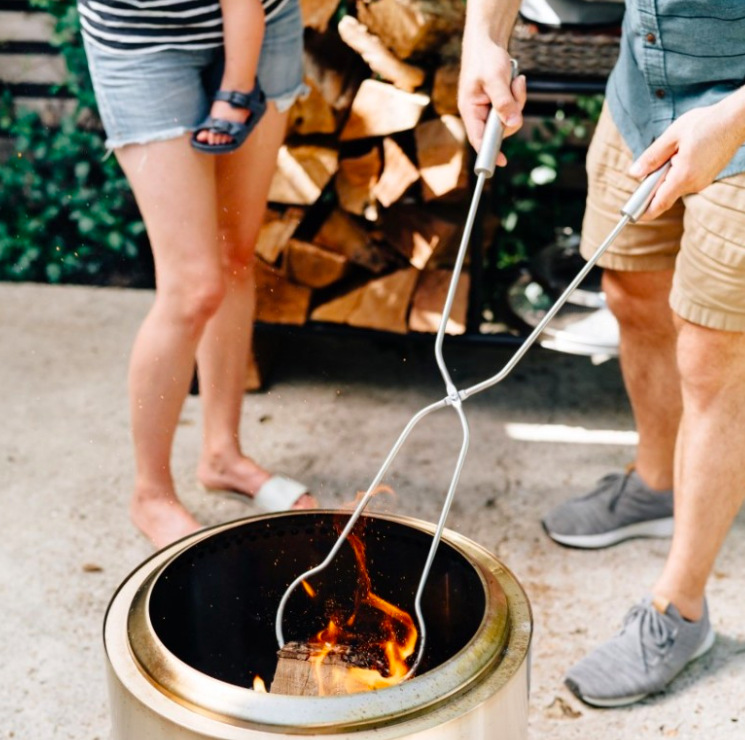 Kliešte zo sady Solo Stove Sticks & Tools pri manipulácii s polenom v záhradnom ohnisku